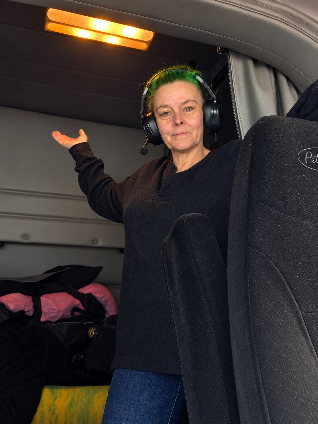 Jessica in the cab of her semi, wearing a headset with one hand raised